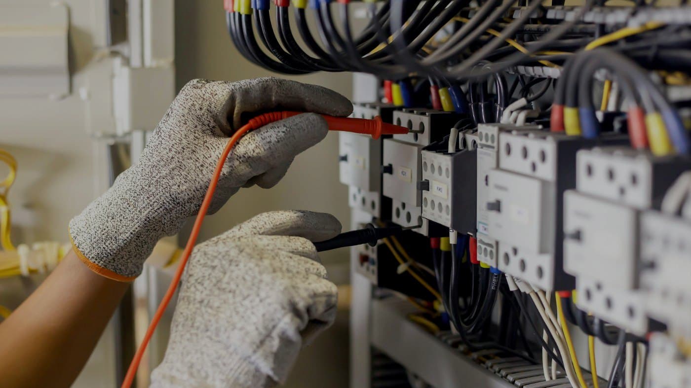 A gloved hand at an open switchboard, circuit breakers and coloured wiring